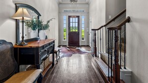 Un couloir avec un bureau en bois, une lampe, un miroir, un tapis en cuir et un escalier.