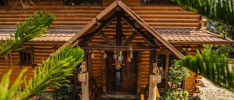 A log cabin with a steeply pitched roof, a central entrance with a wooden door, and a stone pathway leading to the entrance.