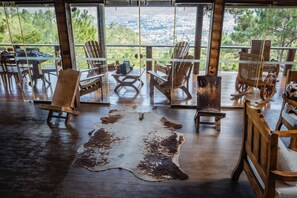 A room with wooden flooring, a large glass window, and several wooden chairs and a rocking chair. - Luxurious Cabin Retreat in Las Jarabacoa With Private Pool, EL Reloj SE Detuvo (Jarabacoa)