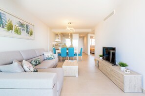 Ein modernes Wohnzimmer mit Sofa, Couchtisch, Fernseher und Essbereich mit Stühlen.
