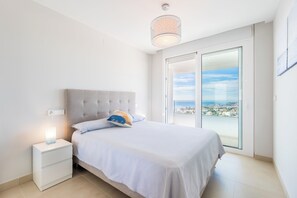 Ein Schlafzimmer mit Bett, Nachttisch und Blick auf die Stadt durch eine Glastür.