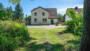 Een huis met twee verdiepingen, een pannendak, een voortuin en een boom aan de rechterkant.