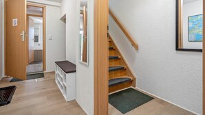 Een hal met een houten deur, een bankje, een trap en een inlijsting kaart aan de muur.