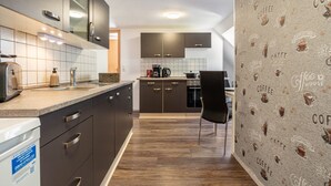 A modern kitchen with dark cabinetry, a built-in oven, and a coffee-themed wall. - Holiday Apartment for 2 People (60 m²) in Wolgast OT Buddenhagen (Wolgast)