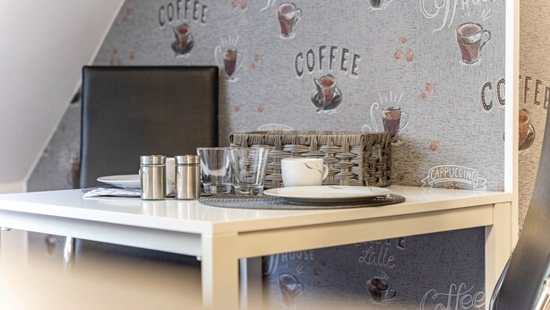 A neatly arranged table with a laptop, glasses, and a cup, set against a wall with a coffee-themed wallpaper. - Holiday Apartment for 2 People (60 m²) in Wolgast OT Buddenhagen (Wolgast)