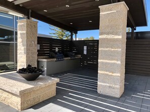 An outdoor patio area with stone columns, a grill station, and a seating area with a bowl of firewood.