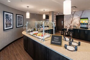 A breakfast bar with a sign offering free daily breakfast, a coffee machine, and framed pictures on the wall.