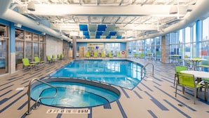 Una piscina interior con sillones y mesas, ventanas amplias y suelo de baldosas.