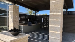 Un patio al aire libre con columnas de piedra, una zona de barbacoa y un área de descanso con un cesto de leña.
