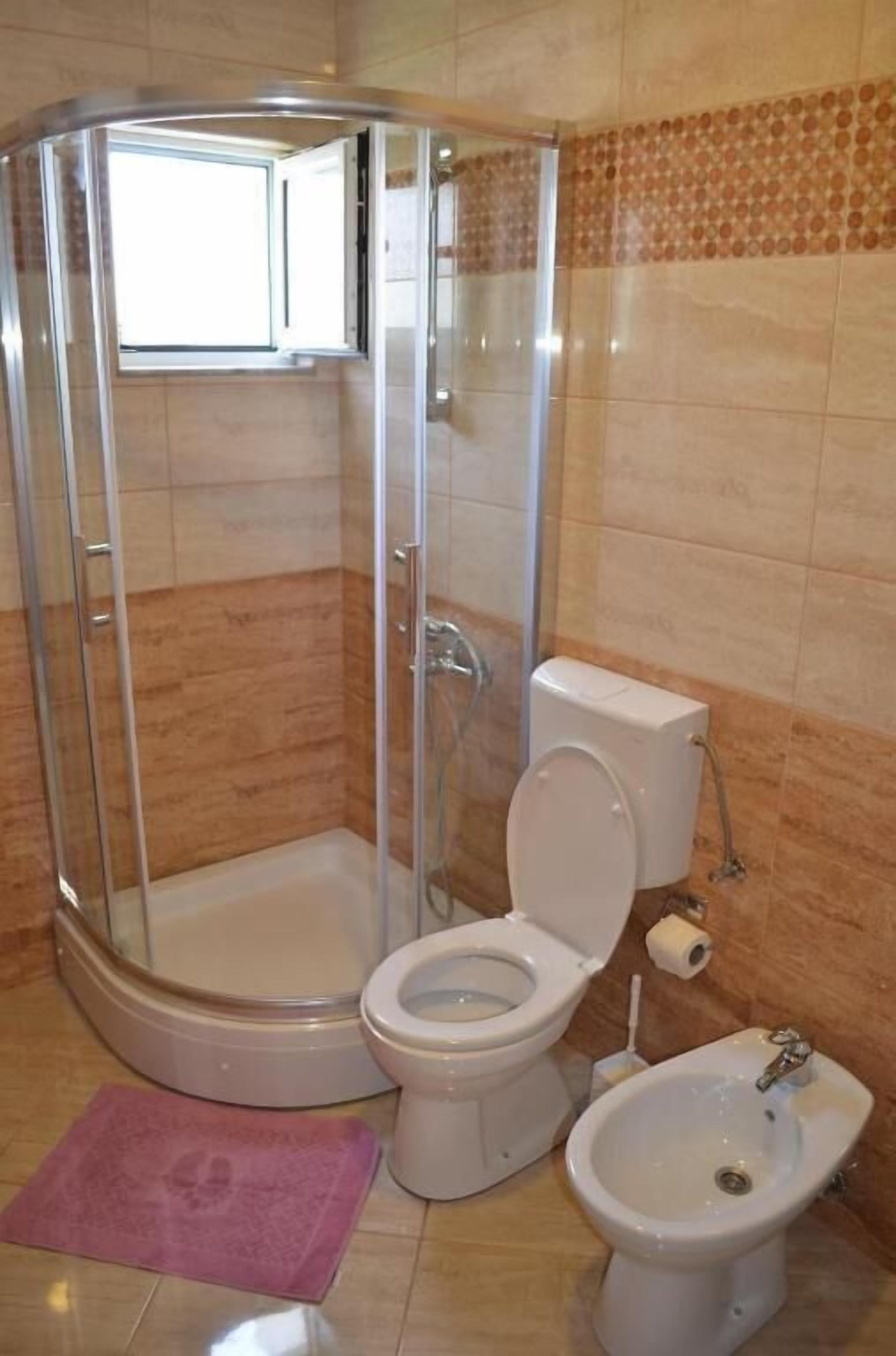 A bathroom with a shower enclosure, toilet, bidet, and a small sink.