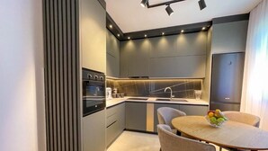 A modern kitchen with a built-in oven, a sink, and a dining area with a round table and chairs. - B&B Lovac  (Ulcinj)