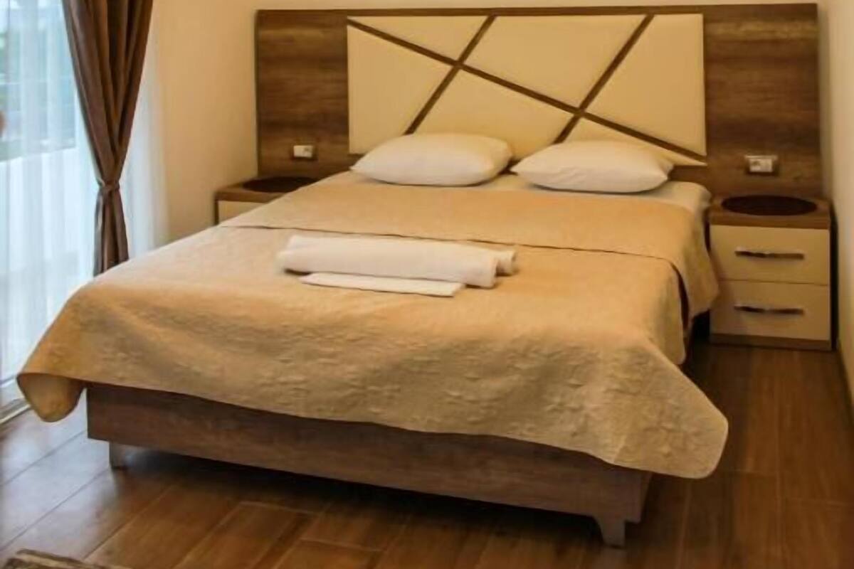 A modern bedroom with a large bed, a headboard with a geometric design, a bedside table, and a wall-mounted artwork.