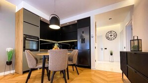 A modern kitchen with a dining area, wooden flooring, and a clock on the wall. - B&B Lovac  (Ulcinj)