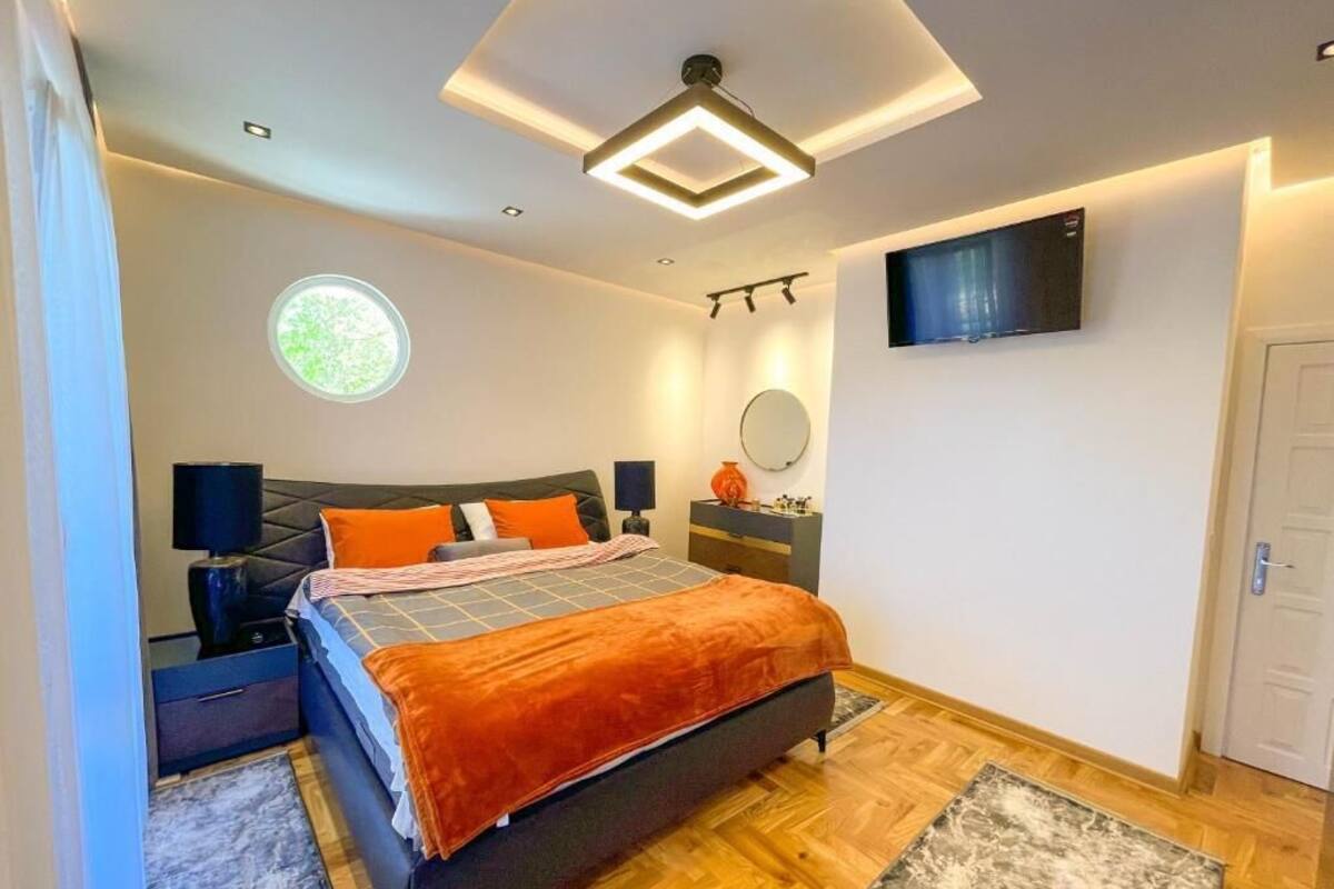 A modern bedroom with a bed, bedside tables, a TV, a round window, and a door.