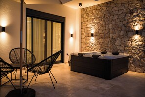 A spa area with a hot tub, stone wall, and two chairs. - B&B Lovac  (Ulcinj)