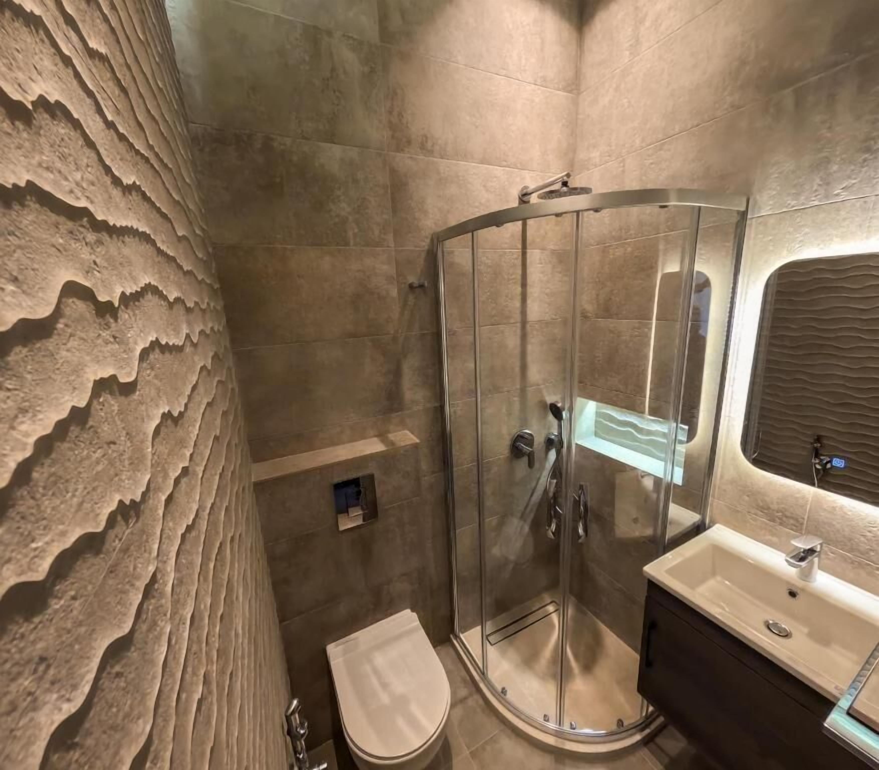 A modern bathroom with a glass-enclosed shower, a toilet, and a sink with a mirror.