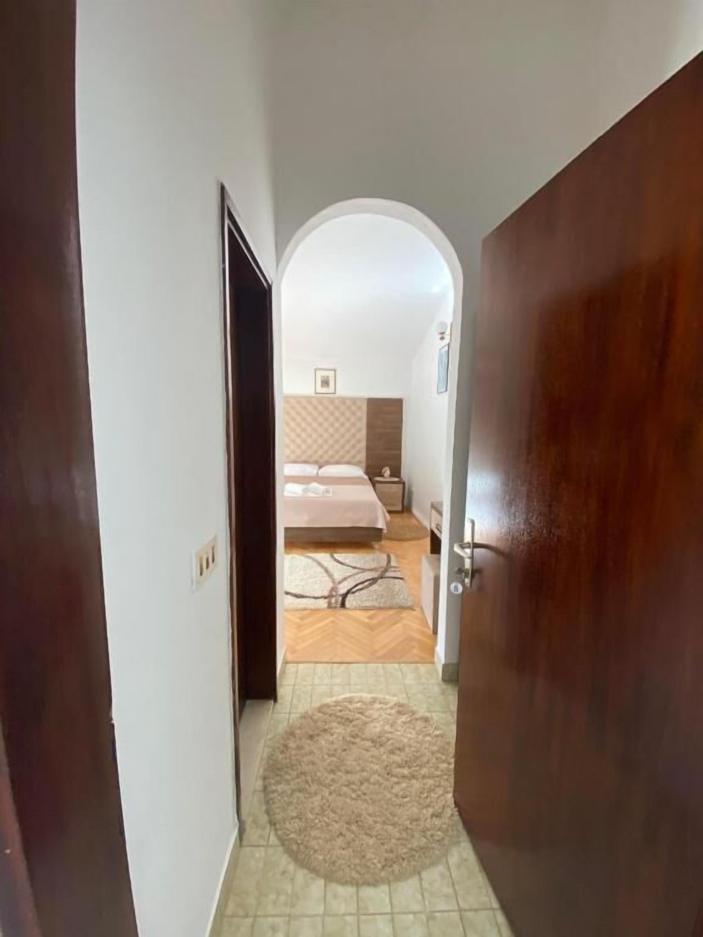 Un pasillo que conduce a un dormitorio con cama, mesita de noche y una alfombra en el suelo.