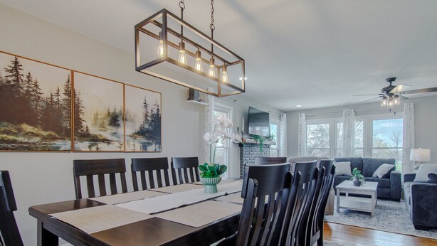 A dining area with a wooden table and chairs, a chandelier, and a painting of a forest scene.
