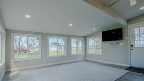 A spacious room with large windows, a flat-screen TV mounted on the wall, and a door with a doormat.