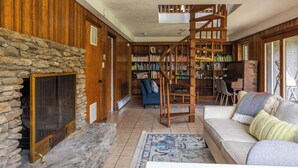 Un accogliente soggiorno con camino in pietra, una scala in legno, una libreria e un pianoforte.
