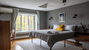 Una camera da letto con un letto, una scrivania, una sedia, una finestra con tende, una ventola a soffitto e una lampada a parete.