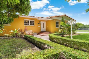 Ein gelbes Haus mit rotem Dach, einer Haustür und einer kleinen Veranda mit einer Bank.