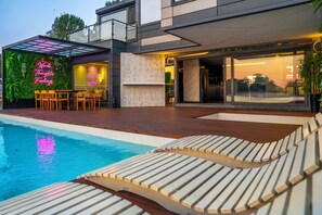 Ein modernes Haus mit Pool, Sitzgelegenheiten im Freien und einer Neonreklame.