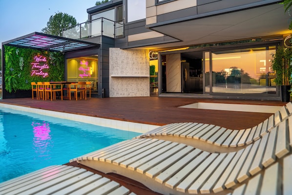 Ein modernes Haus mit Pool, Sitzgelegenheiten im Freien und einer Neonreklame.