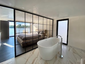 Ein modernes Badezimmer mit einer großen Badewanne, ein Bett mit Seeblick und eine Schiebeglastür.