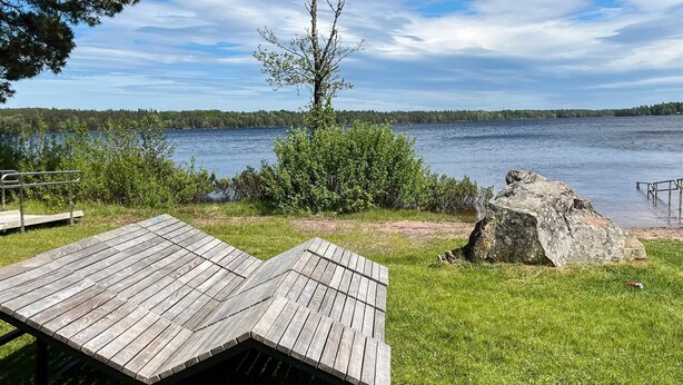 A lakeside view with a wooden deck, a large rock, and a tree. - 5 Person Holiday Home in Kristdala (Kristdala)