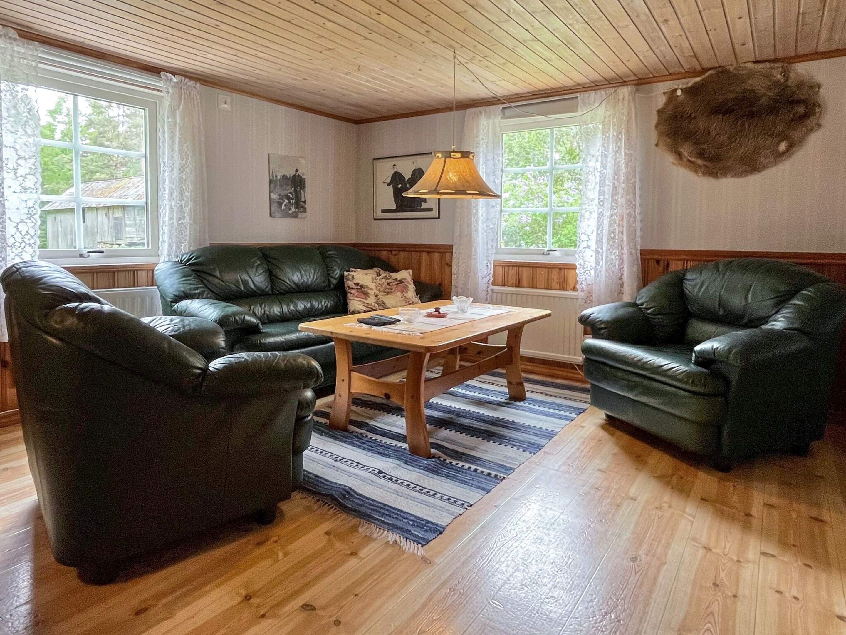 A cozy living room with a wooden ceiling, leather sofas, a wooden coffee table, and a rug.