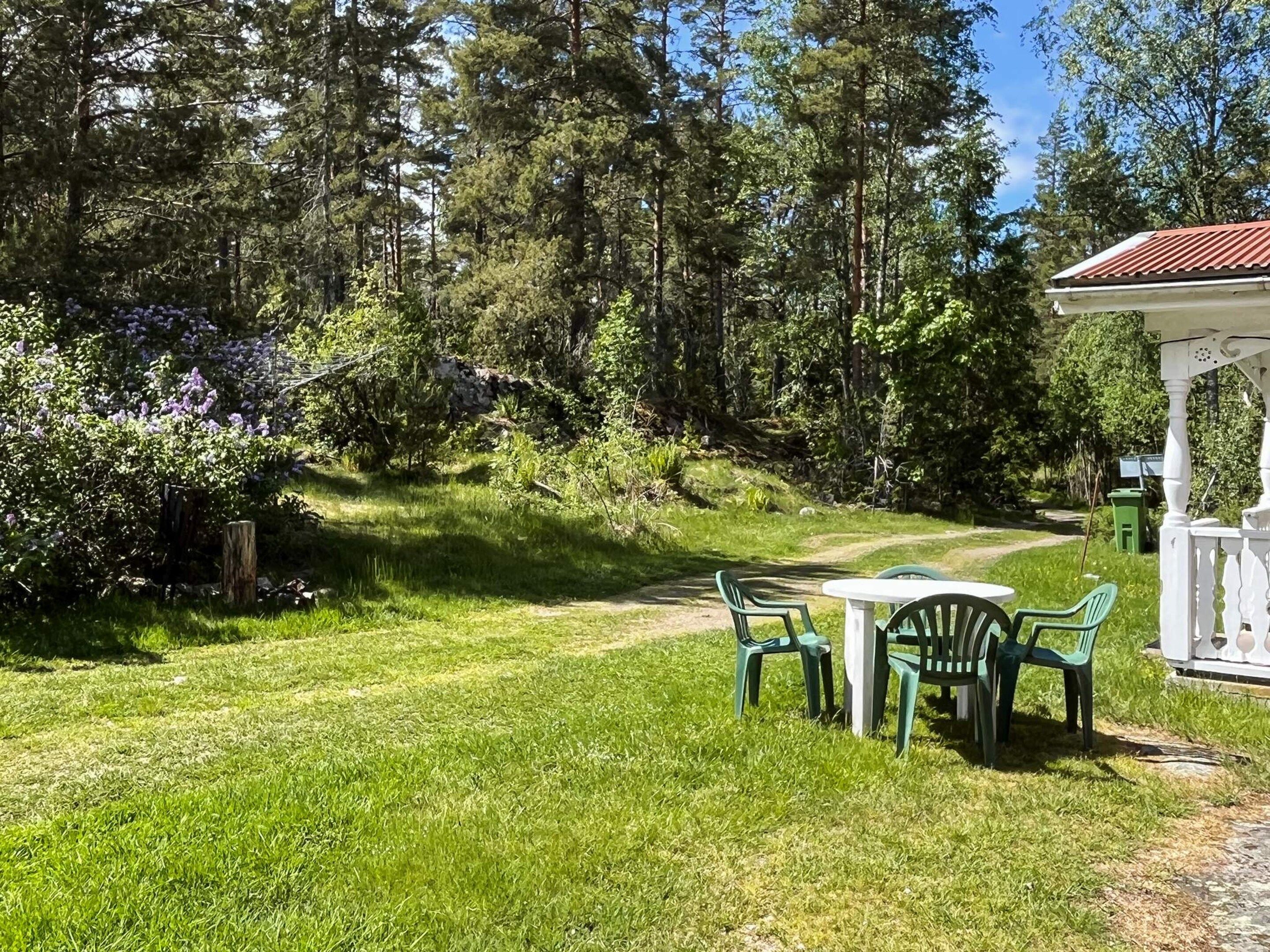 A grassy outdoor area with a white gazebo, green plastic chairs, and a table.
