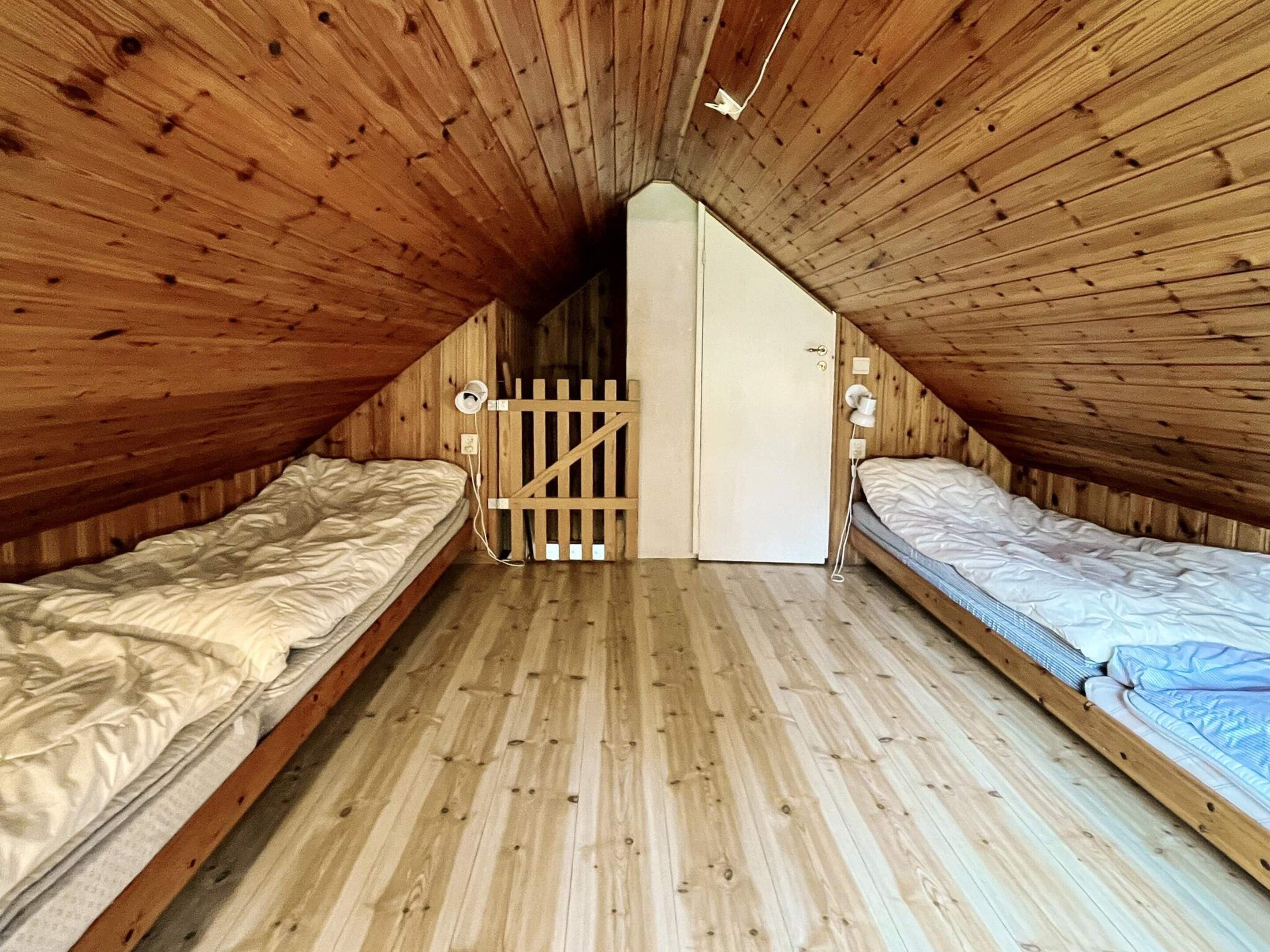 Ein kleines Schlafzimmer im Dachgeschoss mit zwei Betten, Holzwänden und einer geneigten Decke.