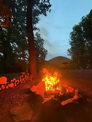 Una fogata con leña y un árbol cercano.