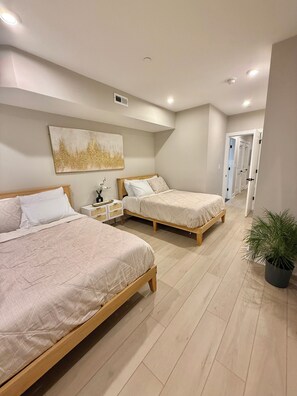 Een slaapkamer met twee bedden, een nachtkastje, een luchtventilator op de muur en een deur die naar een andere kamer leidt.