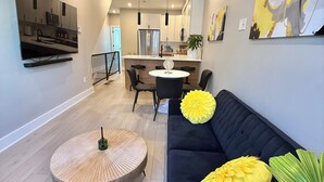Una sala moderna con un sofá negro, una mesa de centro redonda y un comedor con una pequeña isla.
