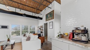 A modern living room with a white sofa, a coffee machine, and a bookshelf. - Cozy industrial loft with rooftop close to FIFA (Atlanta)