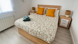 Una cama bien hecha con ropa de cama estampada, dos mesitas de noche con lámparas y un radiador.