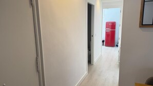 Un pasillo con un refrigerador rojo, paredes blancas y suelo de madera.