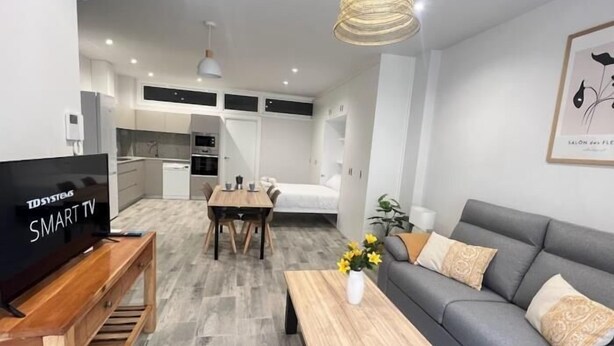 Una sala de estar moderna con televisor, sofá, mesa de comedor y zona de cocina.