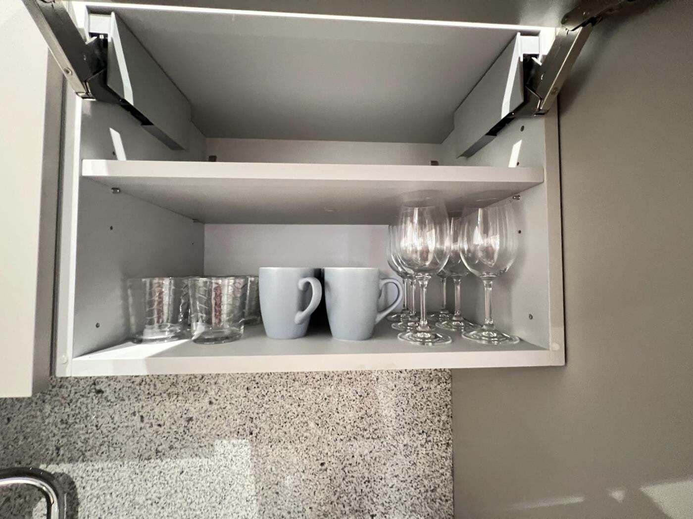 A kitchen cabinet with a built-in shelf containing clear glasses, a white mug, and a clear glass.