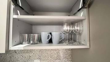 A kitchen cabinet with a built-in shelf containing clear glasses, a white mug, and a clear glass.