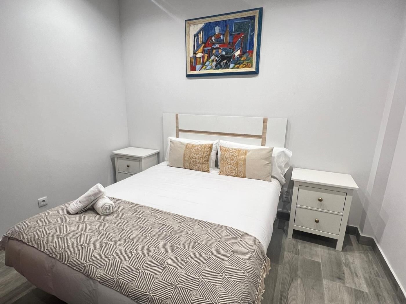 Een slaapkamer met een bed, twee nachtkastjes, een schilderij aan de muur en een bed met een patroon.