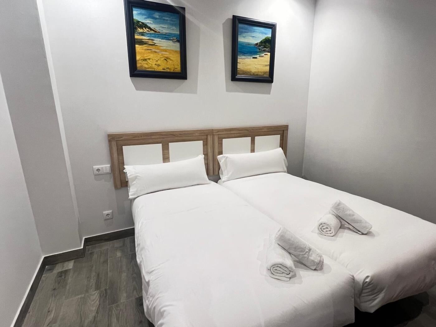 A double bed with white linens, two pillows, and rolled towels on the bed.