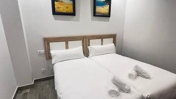 A double bed with white linens, two pillows, and rolled towels on the bed.