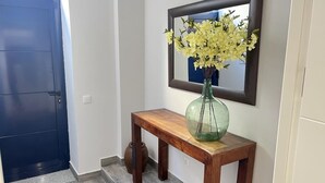 Un pasillo con una puerta azul oscuro, una consola de madera, un jarrón verde con flores y un espejo en la pared.
