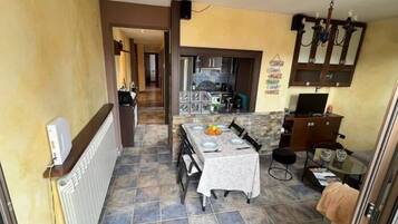 Un pasillo estrecho que lleva a un comedor con una mesa lista para dos personas, una cocina al fondo y un pequeño rincón de descanso con una silla y una mesa.