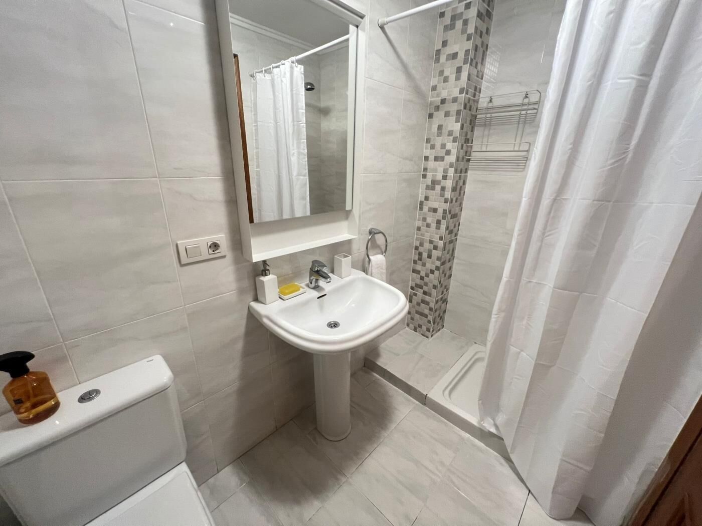 Un baño con inodoro, lavabo, espejo y zona de ducha.