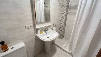 Un baño con inodoro, lavabo, espejo y zona de ducha.