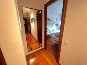 Een gang met een houten vloer die leidt naar een slaapkamer met een stapelbed en een nachtkastje.